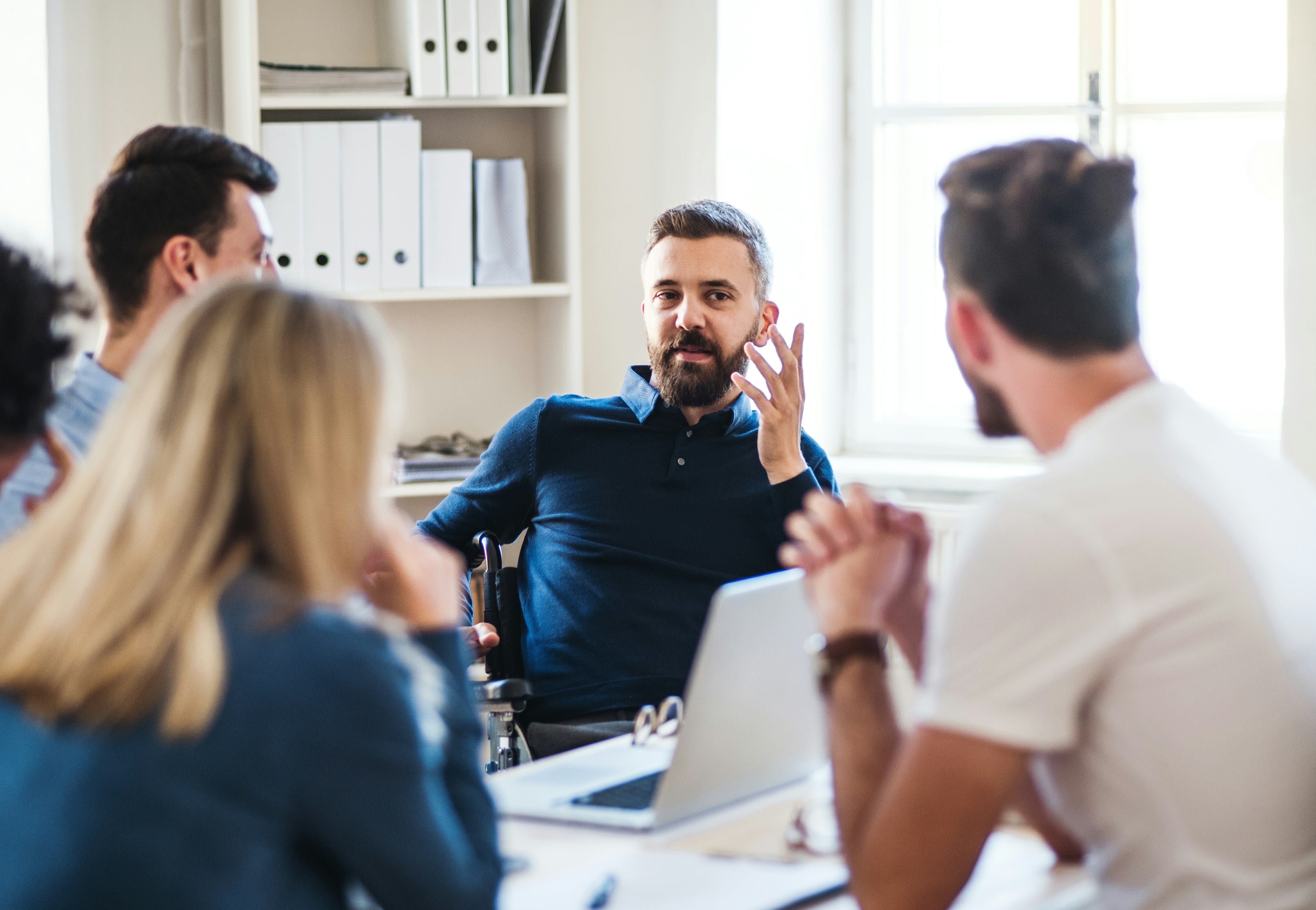 A male department head and perfectionism therapy client contributes to a team
meeting. Staff are in a coworking space and appear engaged in the meeting.